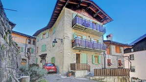 A multi-story building with balconies, a cobblestone street, and a parked car. - Villa Pastoedo Ap. Giallo - Terrace & Mountain Views, Tenno, Italy (Tenno)