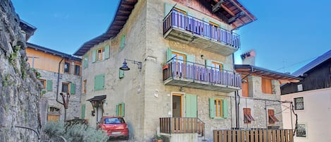 A multi-story building with balconies, a cobblestone street, and a parked car.