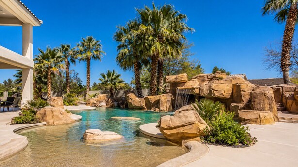 Une piscine d’un complexe hôtelier, avec une eau cristalline, entourée de palmiers et de gros rochers.