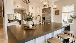 Une cuisine moderne dotée d’un îlot central, de tabourets de bar, de luminaires suspendus et d’appareils électroménagers en acier inoxydable.