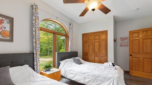 Une chambre avec deux lits, un ventilateur de plafond et une grande fenêtre avec des rideaux.