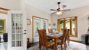 Un coin repas avec une table et des chaises en bois, un ventilateur de plafond et de grandes fenêtres.