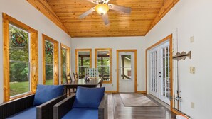 Une pièce meublée de mobilier en osier, dotée de grandes fenêtres, d’un ventilateur de plafond et d’un plancher en bois.