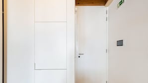 Une porte blanche avec une poignée, un petit panneau indiquant la sortie de secours et un détecteur de fumée fixés au mur.