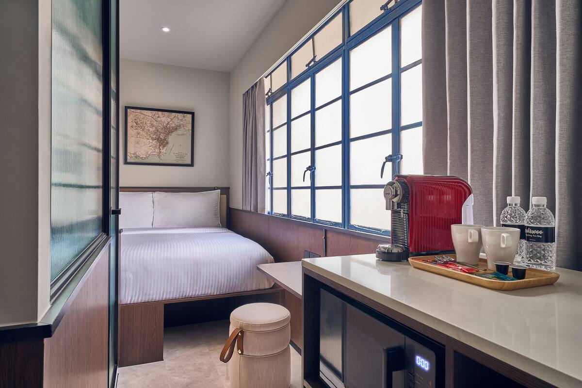 Une chambre d’hôtel compacte comprenant un lit, une petite kitchenette, une fenêtre avec des rideaux et une carte affichée au mur.