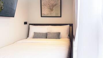 Een netjes opgemaakt bed met twee kussens, een inlijst kaart aan de muur en een raam met gordijnen.