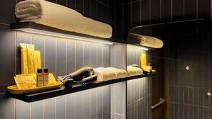 Une salle de bain avec un porte-serviettes sur lequel est pliée une serviette, un sèche-cheveux et des articles de toilette rangés sur une étagère.