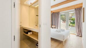 A modern bedroom with a large bed, a bathroom with a mirror and shelves, and a view of the outdoors. - GuestReady - Cedofeita Collection Deluxe P3 (Porto)