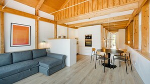 A modern interior with a wooden ceiling, a gray sofa, a dining table with chairs, and a kitchen area. - GuestReady - Cedofeita Collection Deluxe P3 (Porto)