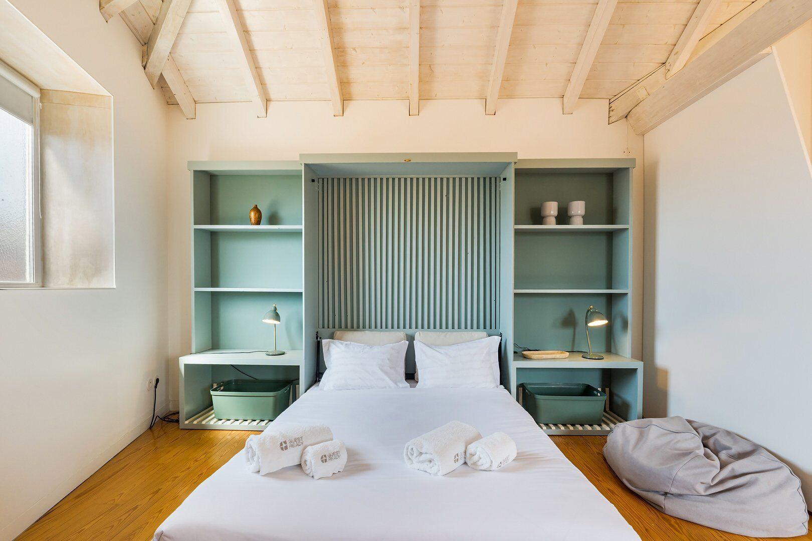 Quarto com cama, duas mesas de cabeceira, encosto e prateleiras embutidas.