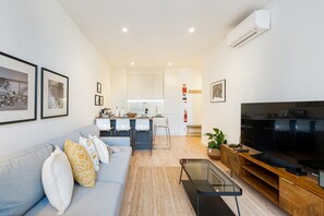 Un salon moderne avec un canapé, un téléviseur et un coin cuisine à l’arrière-plan.