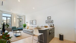 Een moderne keuken met een centraal eiland, een zithoek met een bank en stoelen, en een groot raam dat zorgt voor natuurlijk licht.