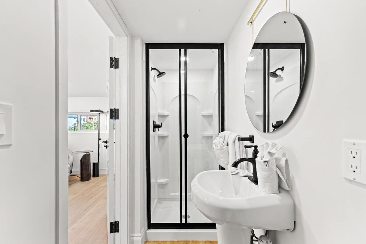 A modern bathroom with a white sink, a round mirror, and a glass shower enclosure.
