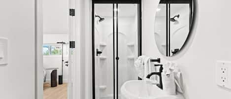 A modern bathroom with a white sink, a round mirror, and a glass shower enclosure.