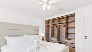 A hotel room with a large bed, a ceiling fan, a walk-in closet with wooden shelves, and a bedside table with a lamp.