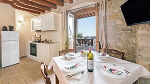 Un comedor con una mesa preparada para dos personas, una botella de vino y vistas al exterior a través de una puerta abierta.