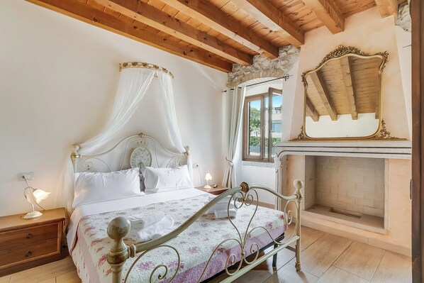 A bedroom with a four-poster bed, a stone fireplace, and a view of the outdoors.
