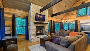 A cozy cabin interior with a stone fireplace, a large sofa, and a television mounted above it.