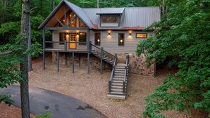 A cabin with a stone foundation, a wooden deck, and a staircase leading to the entrance.