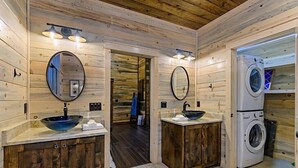 Een houten badkamer met twee wastafels, een spiegel, een wasmachine en een houten kast.