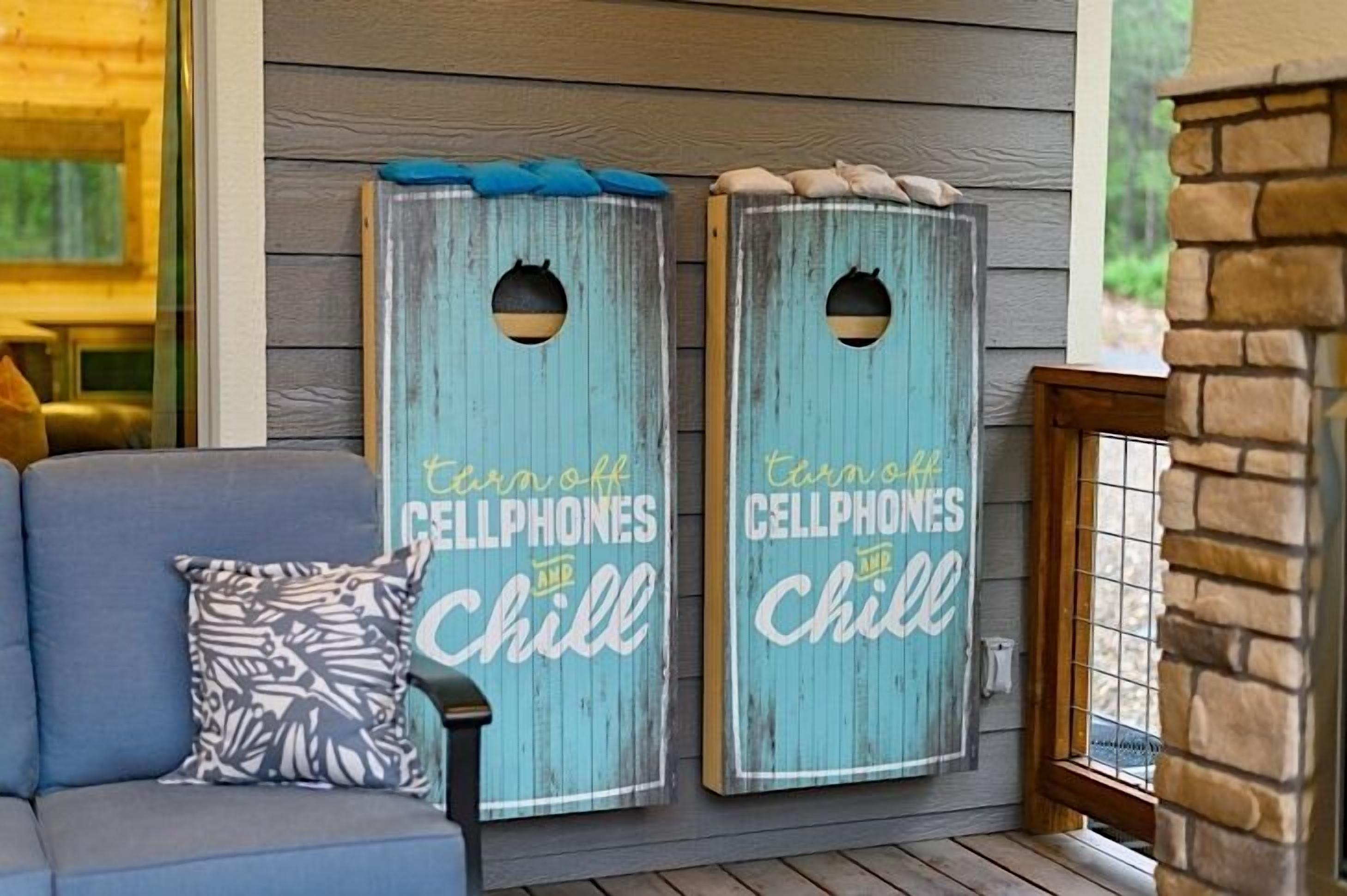 Two wooden signs with 'turn off cellphones and chill' written on them, placed on a porch with a couch and a patterned pillow.