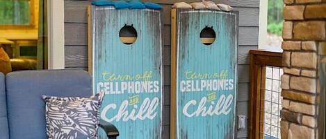 Two wooden signs with 'turn off cellphones and chill' written on them, placed on a porch with a couch and a patterned pillow.