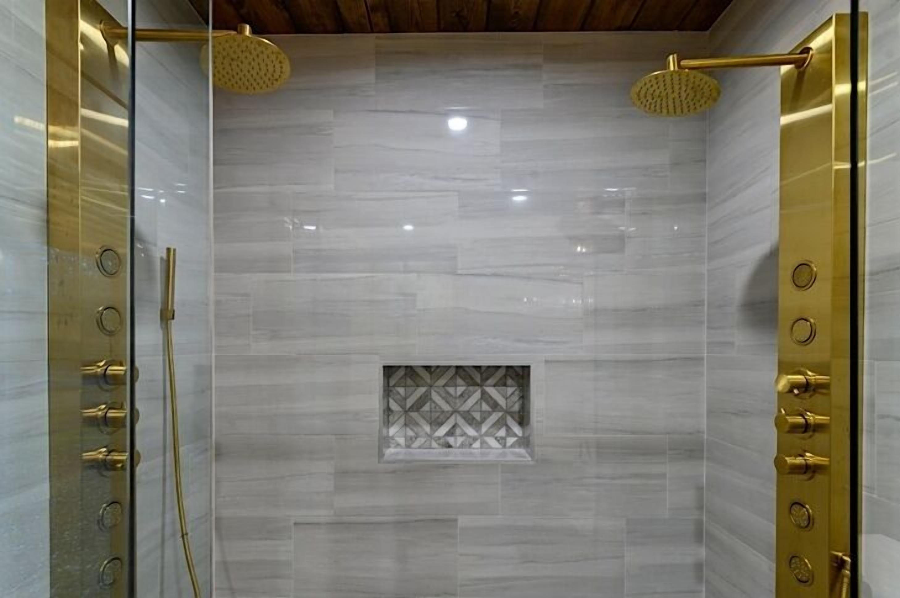 A walk-in shower with a glass door, a gold handle, and a showerhead.