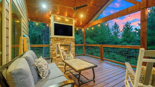 Una terraza de madera con chimenea de piedra, asientos exteriores y un televisor montado en la pared.