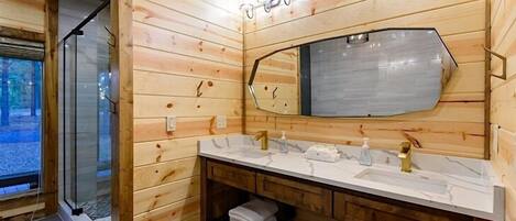 A wooden cabin bathroom with a large mirror, two sinks, and a glass shower enclosure.