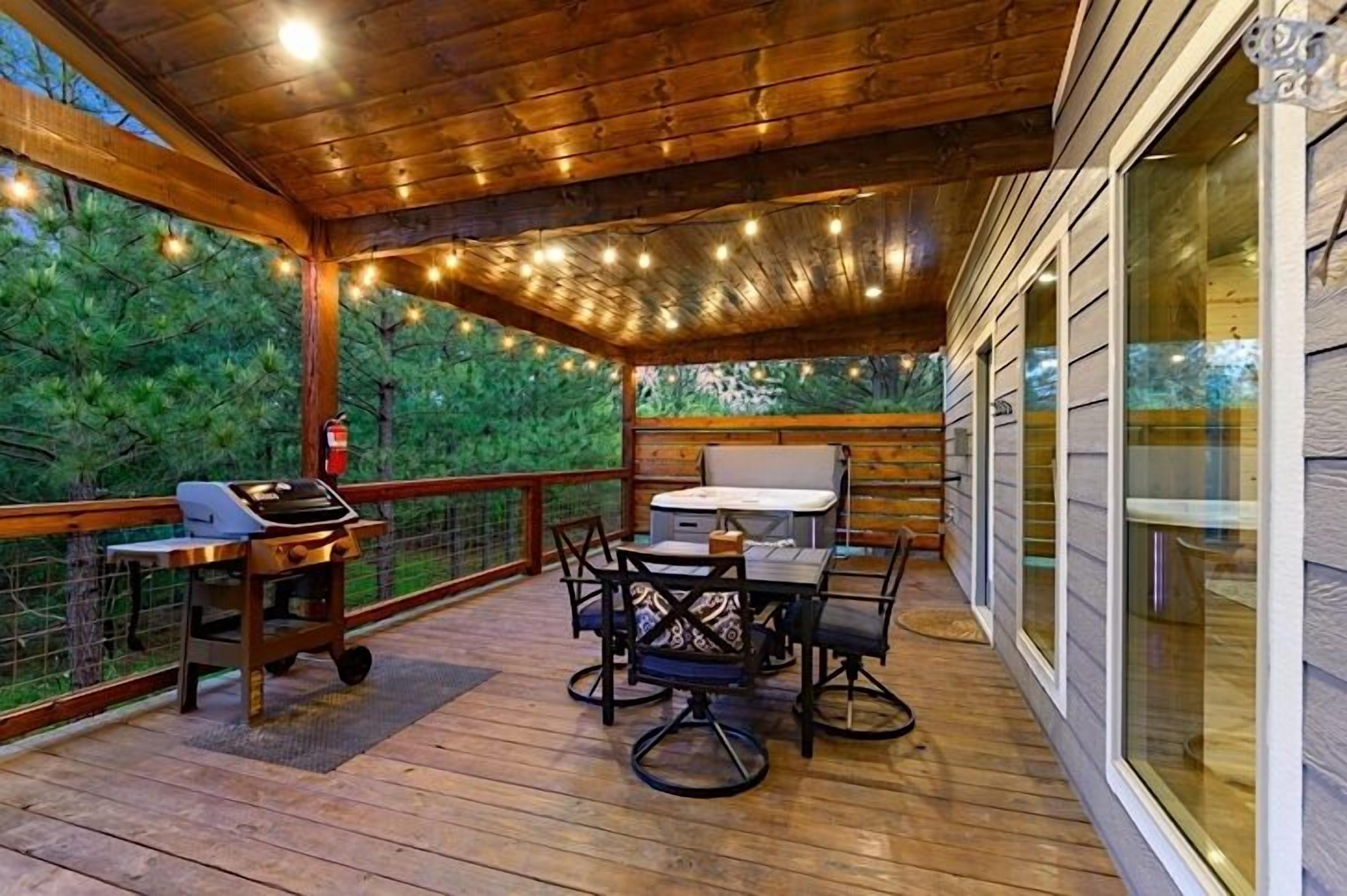 A covered deck with a grill, dining table, and chairs, surrounded by glass windows and wooden railings.