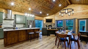 Una cocina amplia con armarios de madera, una isla central con taburetes y un comedor con mesa dispuesta para cuatro personas.