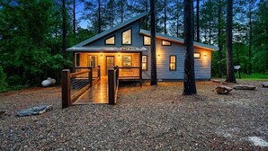 Une cabane moderne dotée d’une terrasse en bois et d’un portail en métal, entourée d’arbres.