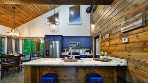 Une cuisine moderne avec des murs en bois, un grand îlot central et des tabourets de bar bleus.