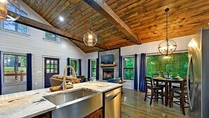 Une cuisine moderne dotée d’un grand îlot central, d’un plafond en bois et d’un coin repas agrémenté d’une cheminée.