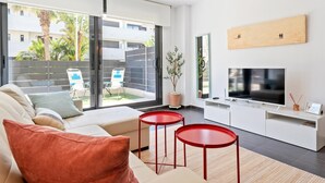A modern living room with a sofa, two red side tables, a TV, and a large window overlooking a courtyard.