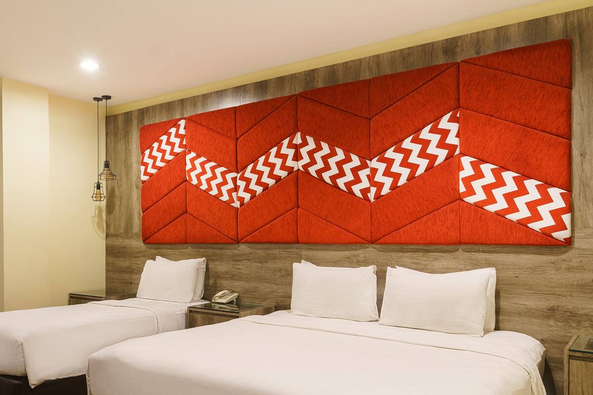 Une chambre d’hôtel avec deux lits, une tête de lit en bois et un panneau mural rouge à motifs géométriques.
