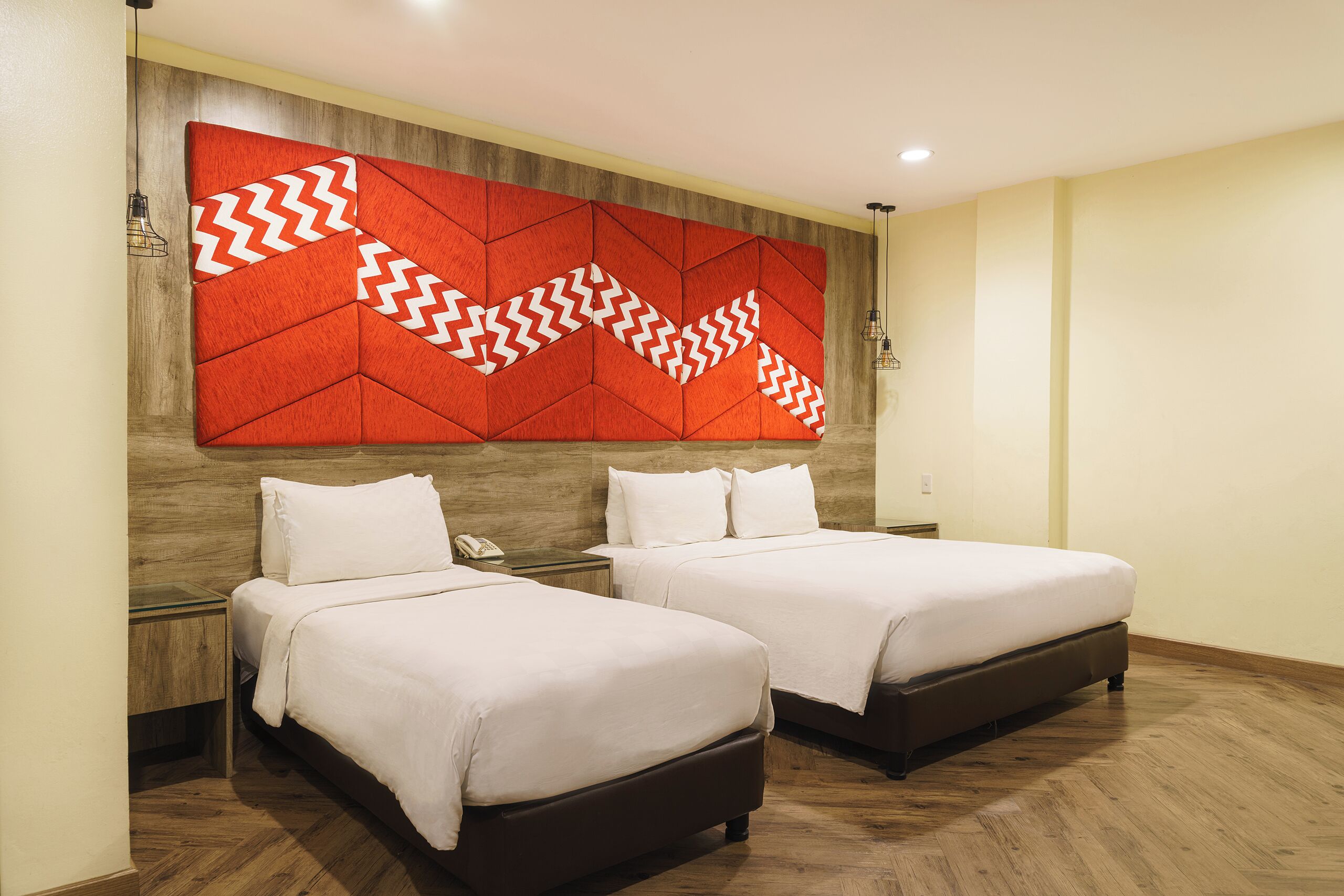 A hotel room with two beds, wooden headboard, and a red geometric wall decoration.