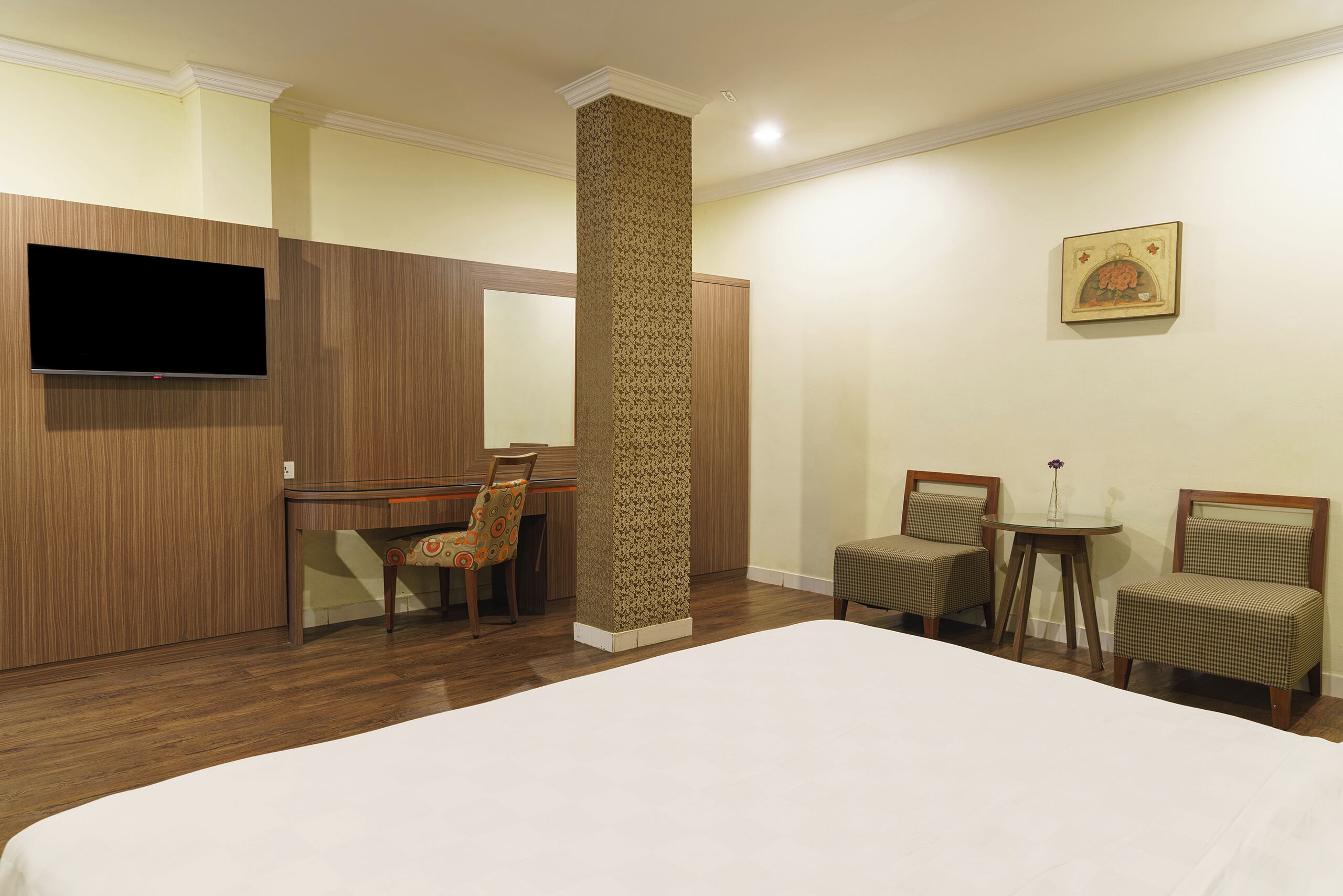 Una habitación de hotel con una cama, un escritorio, dos sillas, un televisor y un cuadro en la pared.