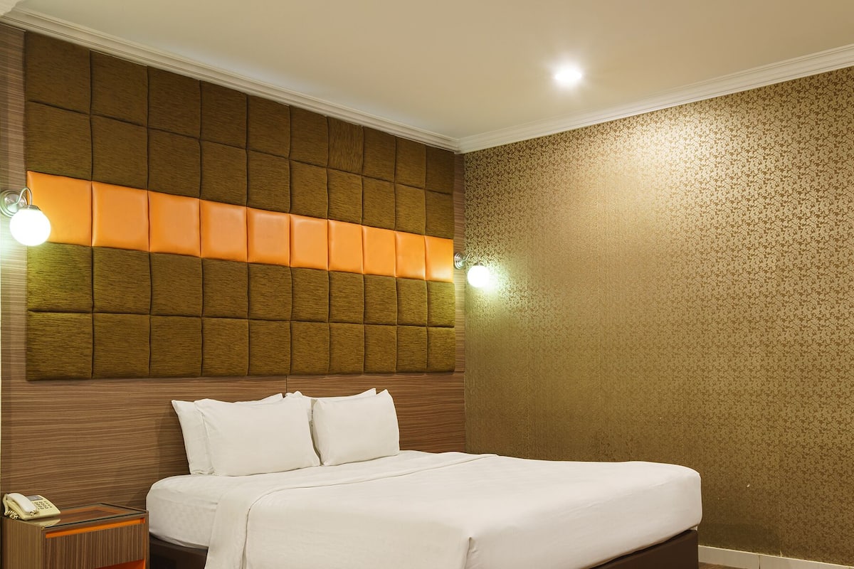 Une chambre d’hôtel avec un lit, une tête de lit dotée d’un panneau lumineux, un mur à motifs et une table de chevet avec un téléphone.