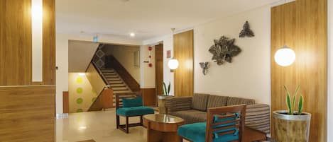 A modern living area with a sofa, two armchairs, a coffee table, and a potted plant. A staircase is visible in the background.