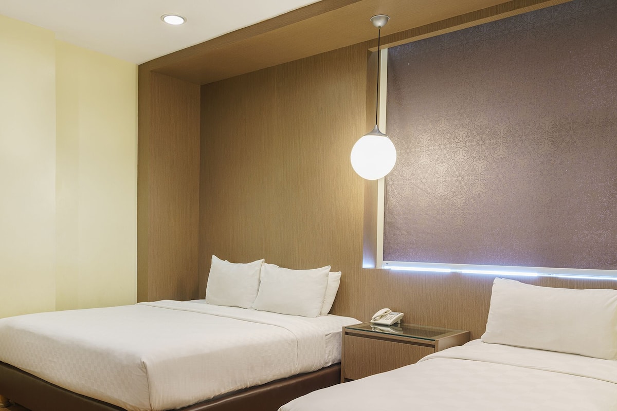 Une chambre d’hôtel avec deux lits, une table de chevet avec un téléphone et une fenêtre avec un luminaire.