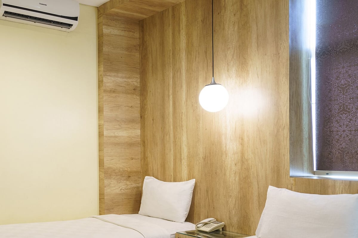 Une chambre d’hôtel avec un mur d’accent en bois, un lit avec une literie blanche, une table de chevet avec un téléphone et une fenêtre ornée d’un rideau à motifs.