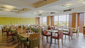 Un comedor amplio con múltiples mesas y sillas, ventanas grandes con persianas y un diseño de techo moderno.