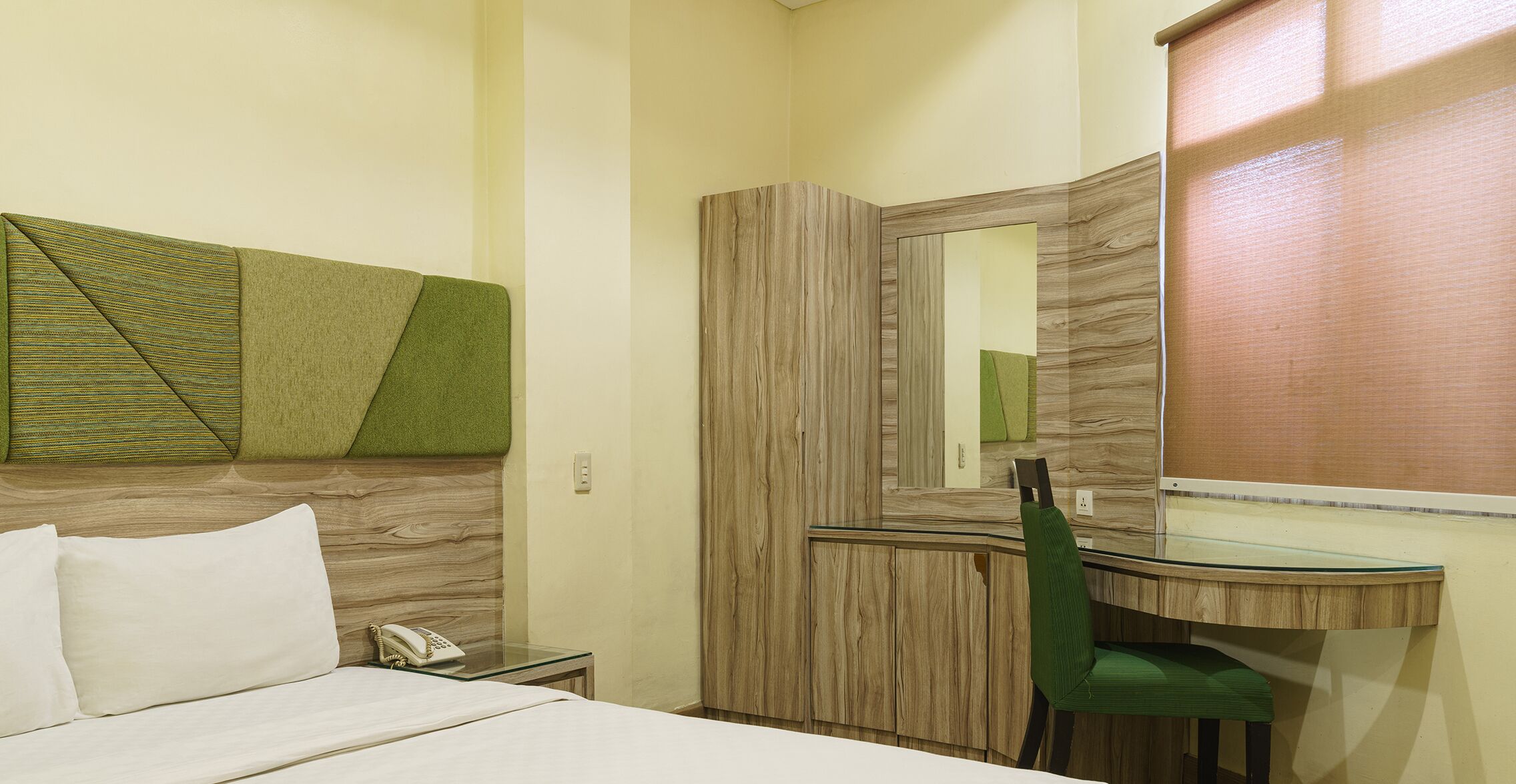 A hotel room with a bed, a desk with a chair, a mirror, and a telephone.