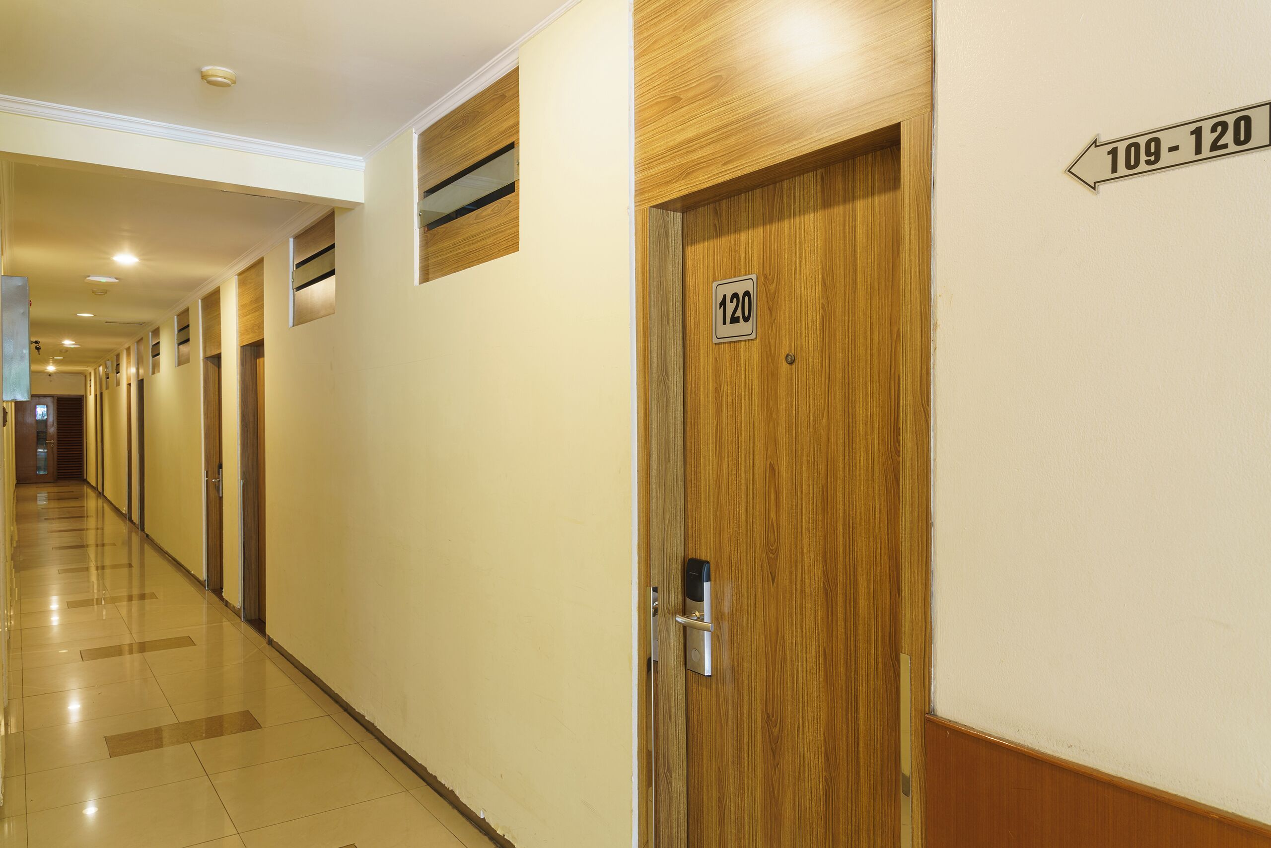 A hotel hallway with doors numbered 109-120, a wooden door with a lock, and a sign indicating the room numbers.