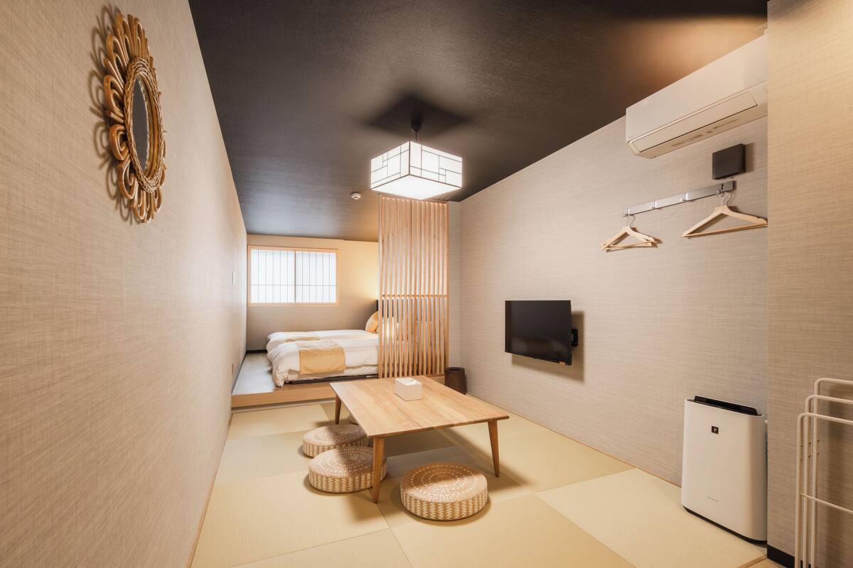 Una habitación minimalista con suelo de tatami, una mesa de madera baja, una lámpara colgante, una cama con vistas y un televisor montado en la pared.