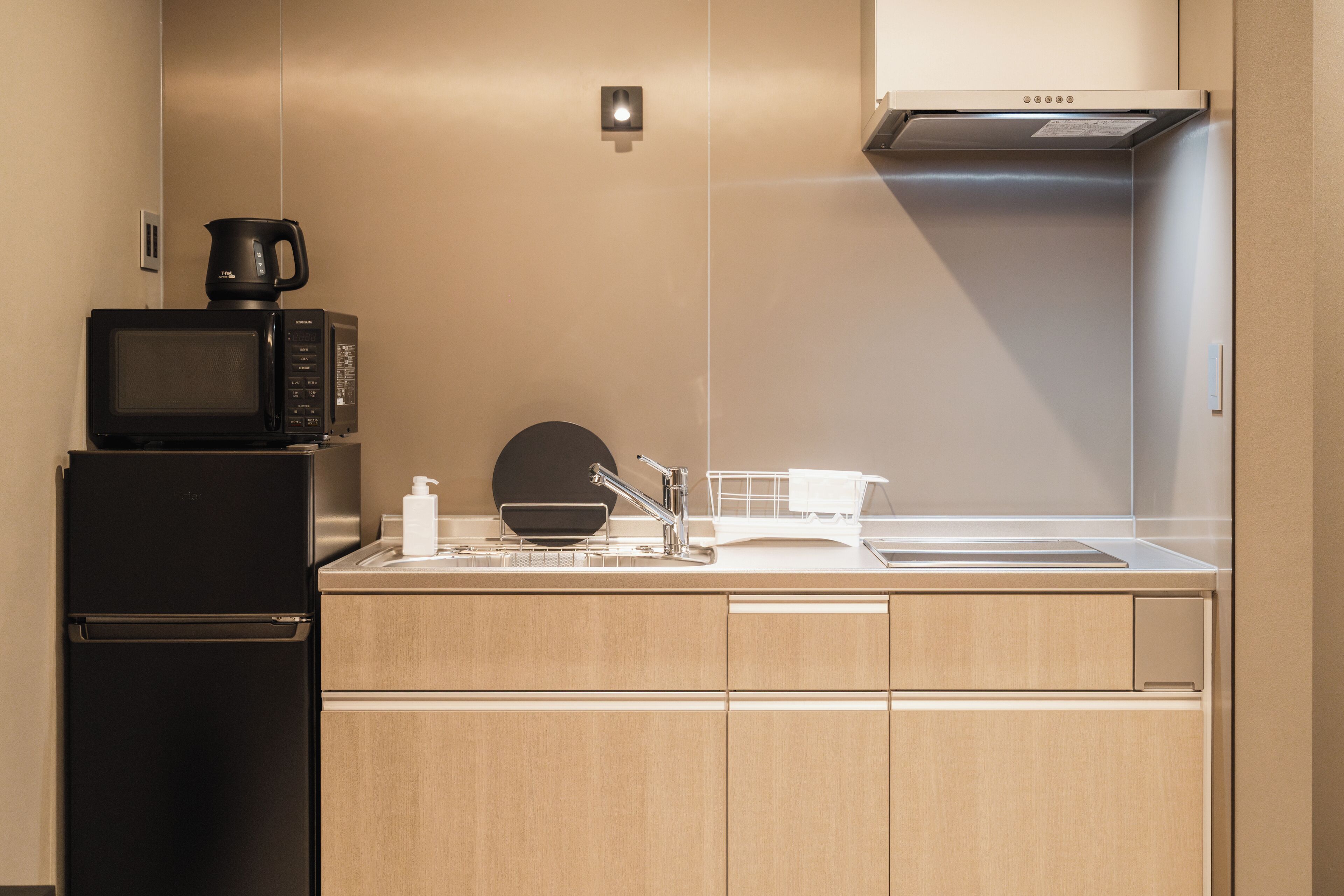 A compact kitchen with a black refrigerator, a microwave, a coffee maker, a sink, and a white countertop.