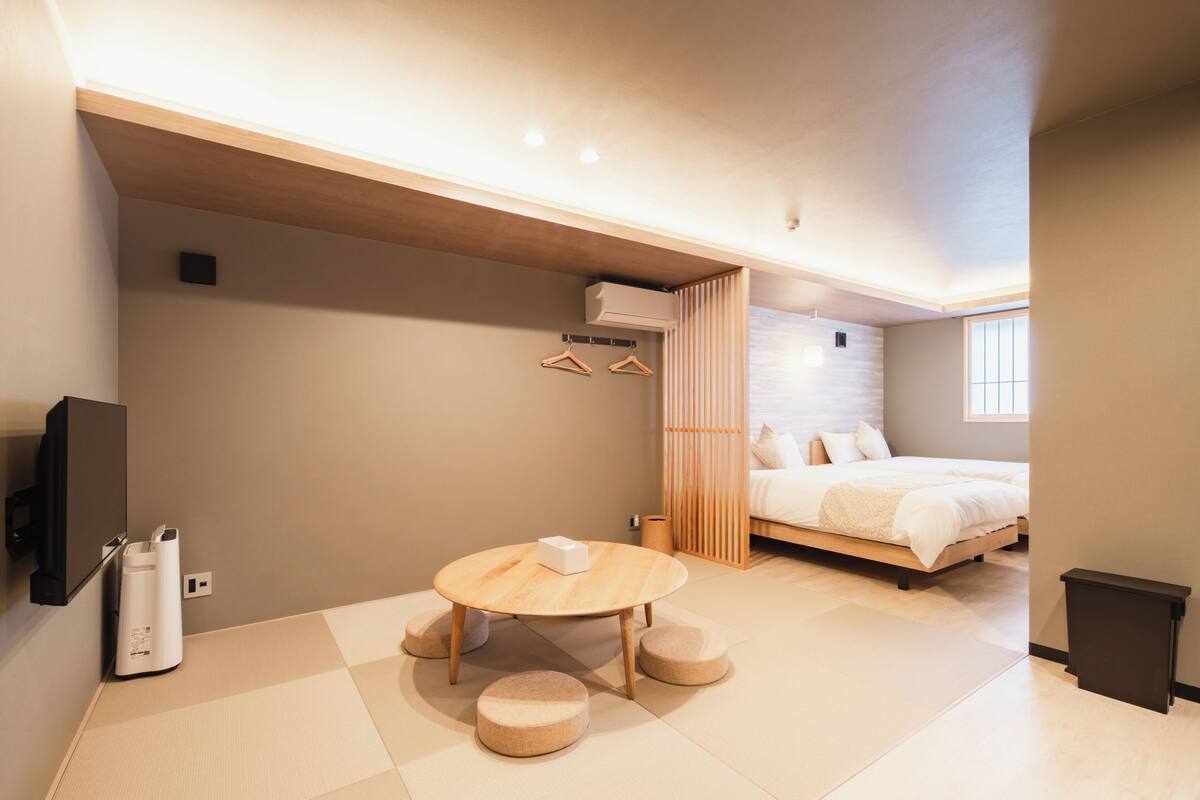 Un dormitorio moderno con cama, una mesa de madera con cojines, televisión y aire acondicionado instalado en la pared.