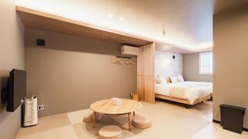 A modern bedroom with a bed, a wooden table with cushions, a TV, and a wall-mounted air conditioner.