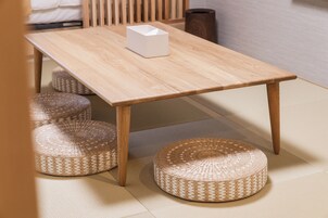 Uma mesa de madeira com um objeto branco sobre ela, rodeada por banquinhos trançados.